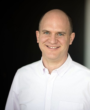 Picture of Ben, wearing a lightly-coloured collared shirt with a black background.